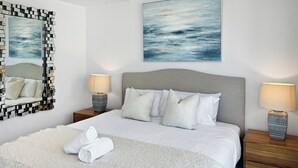 A neatly made bed with white linens, a grey headboard, and a white throw blanket. There are two bedside tables with lamps and a large abstract painting above the bed. - Unit 2907 Oracle Tower 1 Level 29 (Broadbeach)