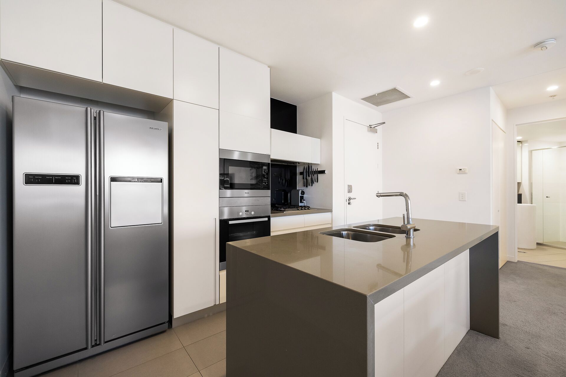 A modern kitchen with a stainless steel refrigerator, built-in oven, microwave, and a large island with a sink.