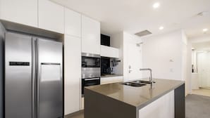 A modern kitchen with a stainless steel refrigerator, built-in oven, microwave, and a large island with a sink. - Unit 2907 Oracle Tower 1 Level 29 (Broadbeach)