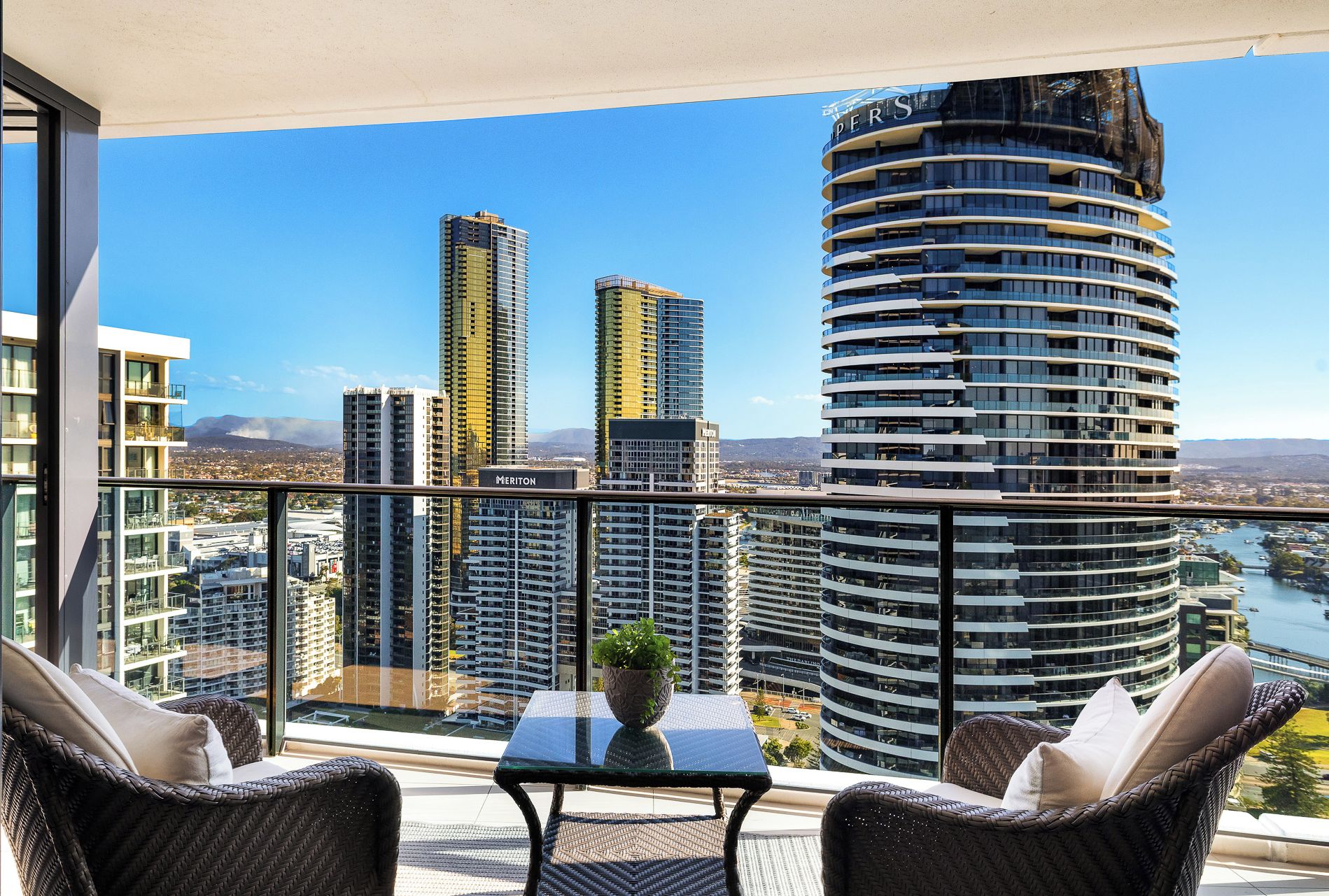 Un balcón con muebles de mimbre, una mesita con una planta y vistas a edificios altos y un río.