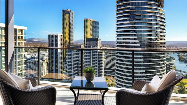 A balcony with wicker furniture, a small table with a plant, and a view of high-rise buildings and a river. - Unit 2907 Oracle Tower 1 Level 29 (Broadbeach)