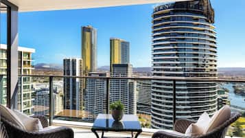 A balcony with wicker furniture, a small table with a plant, and a view of high-rise buildings and a river.