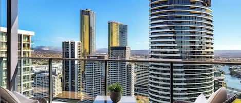 Un balcón con muebles de mimbre, una mesita con una planta y vistas a edificios altos y un río.