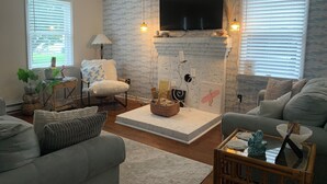 Un salon doté d’une cheminée, d’un téléviseur fixé au-dessus, et d’un coin salon confortable avec un canapé et des fauteuils.
