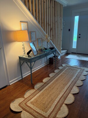 Un escalier avec une rampe en bois, un bureau avec une lampe, des tableaux encadrés et un vase rempli de fleurs.