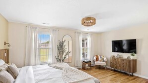 Un dormitorio con una cama, televisor, aparador de madera y una ventana con cortinas.