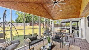 Un patio techado con mobiliario exterior, ventilador de techo y vista al jardín trasero.