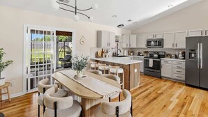 Una cocina moderna con armarios blancos, una isla central y un comedor con mesa y sillas de madera.