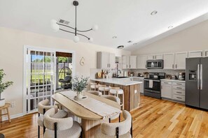 A modern kitchen with white cabinets, a central island, and a dining area with a wooden table and chairs. - Private GEM in SC-Pool, Huge Porch, Fenced Yard (Greer)