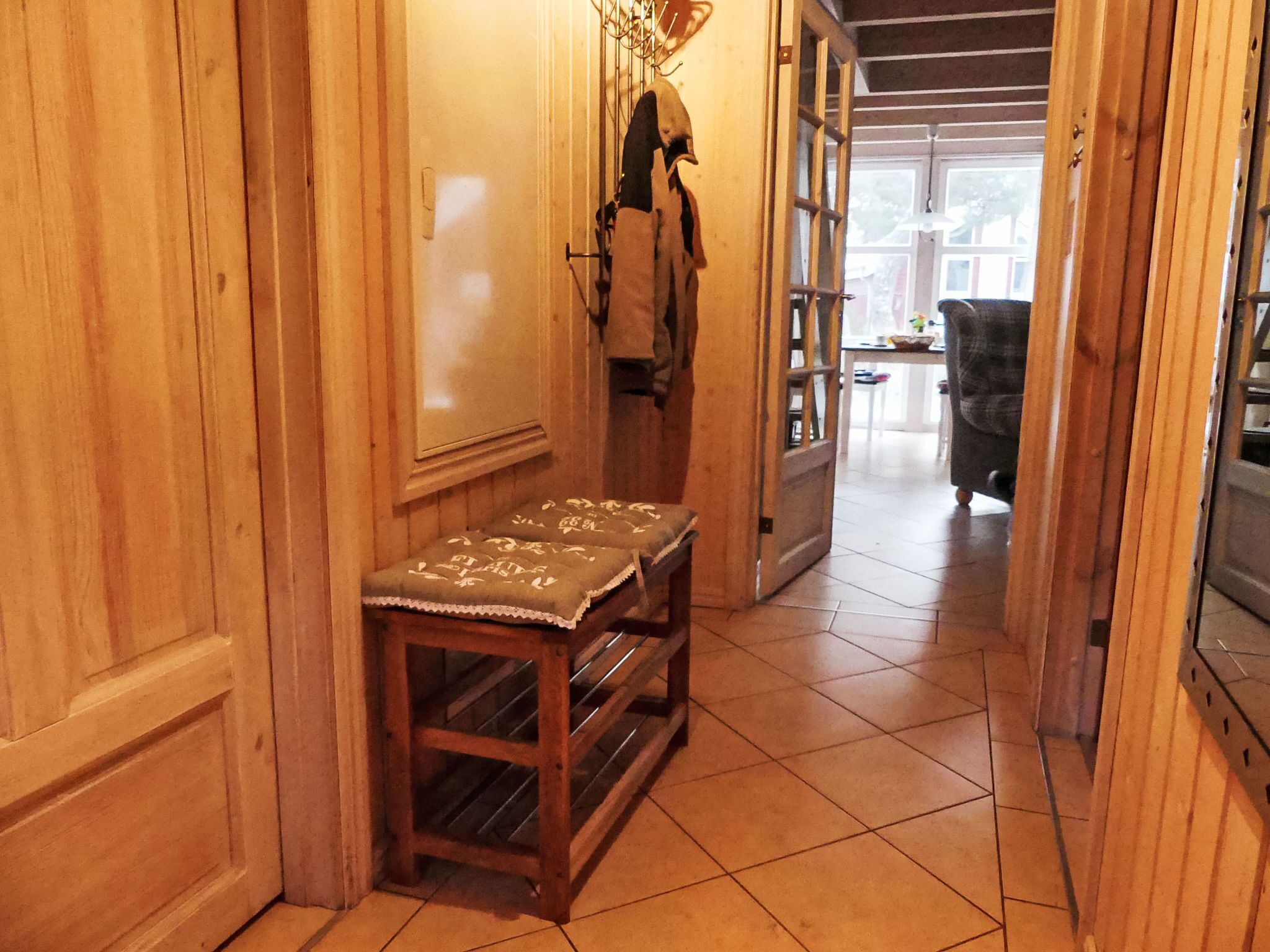 A wooden interior with a bench, a coat rack, and a door leading to another room.