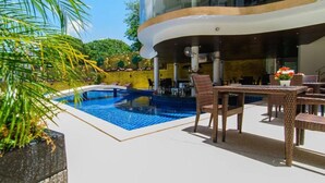 Area piscina moderna all'aperto con struttura a forma di curva, sedie a sdraio e tavolo da pranzo.
