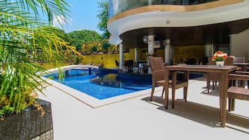 Un espace piscine extérieur moderne, doté d’une structure incurvée, de chaises longues et d’une table à manger.