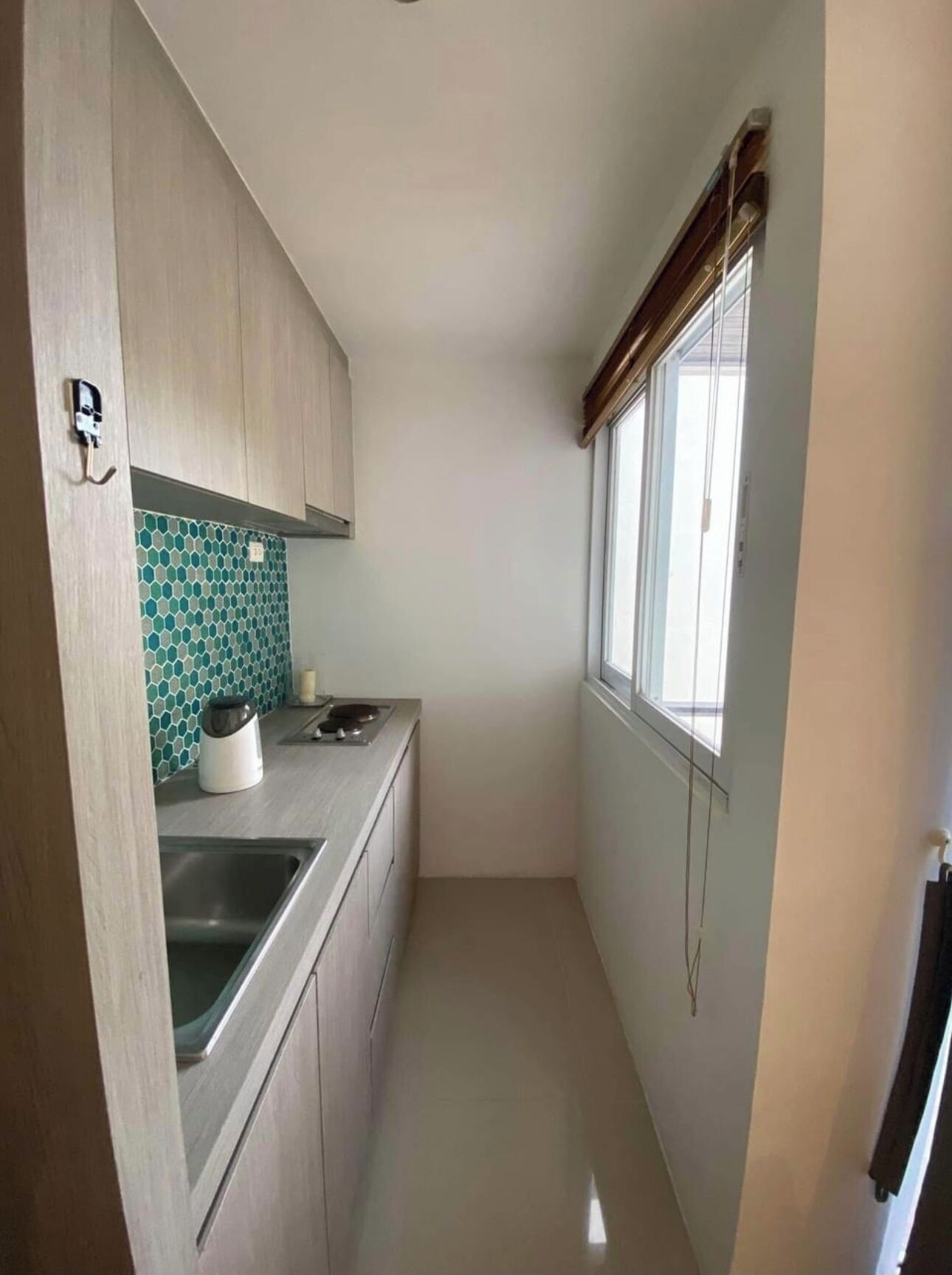 A narrow kitchen with wooden cabinets, a tiled backsplash, a window, and a stainless steel sink.