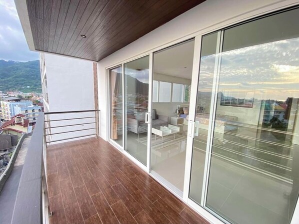 A balcony with a wooden floor and glass doors leading to a living area with a sofa and coffee table.