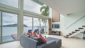 Una sala de estar moderna con un amplio ventanal corredera que da a un balcón con vistas a una masa de agua y colinas.