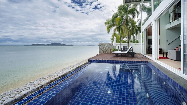 Una piscina moderna con baldosas azules, un muro de piedra y vista al mar.