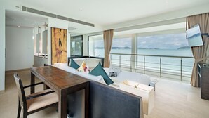 Una habitación de hotel moderna con un ventanal que ofrece vistas al mar, una mesa de comedor de madera, una cama con vistas y un televisor montado en la pared.