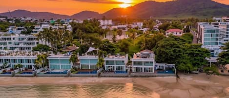A coastal resort with modern buildings, a beach, and a sunset.