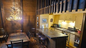 A cozy dining area with a wooden table and chairs, a bar with stools, and a kitchen with a stove and microwave. - The Cub House: Mountain Home w/ Hot Tub, Pool Table, 5 bed/4ba, Fireplace, Woods (Ruidoso)
