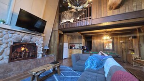 A cozy cabin interior with a stone fireplace, a flat-screen TV, a pool table, and a dining area. - The Cub House: Mountain Home w/ Hot Tub, Pool Table, 5 bed/4ba, Fireplace, Woods (Ruidoso)