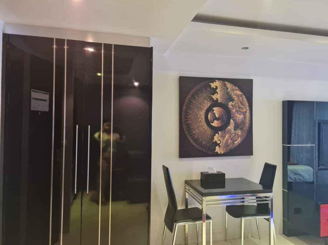 Un espace repas moderne avec une table et des chaises en verre, un élément décoratif mural et une porte coulissante donnant sur une autre pièce.
