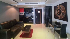 A modern living room with a sofa, a coffee table, and a dining area with a table and chairs. There is a kitchen area with cabinets and a microwave. - L02 Bangla Suites, Modern Studio On Bangla Road (Patong)