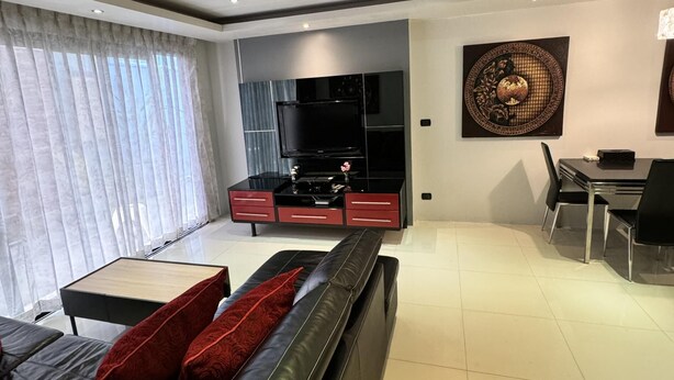 A modern living room with a black leather sofa, a flat-screen TV, a dining area with a table and chairs, and a decorative wall piece. - L08 Penthouse Suite, Modern Condo On Bangla Road (Patong)