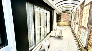A corridor with a glass ceiling, a brick wall, and a small seating area with stools. - L08 Penthouse Suite, Modern Condo On Bangla Road (Patong)