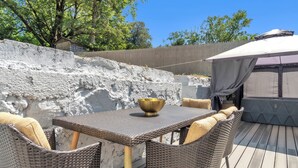 Un patio con mobiliario de mimbre, una mesa y una zona cubierta.