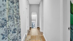 Un pasillo estrecho con suelo de madera, paredes blancas y una cortina estampada con motivos florales a la izquierda.