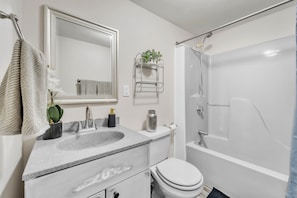 A modern bathroom with a white sink, mirror, toilet, and bathtub.