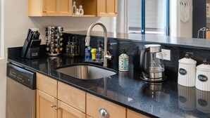 Een moderne keuken met een RVS spoelbak, houten kastjes, een koffiezetapparaat en diverse keukengerei.