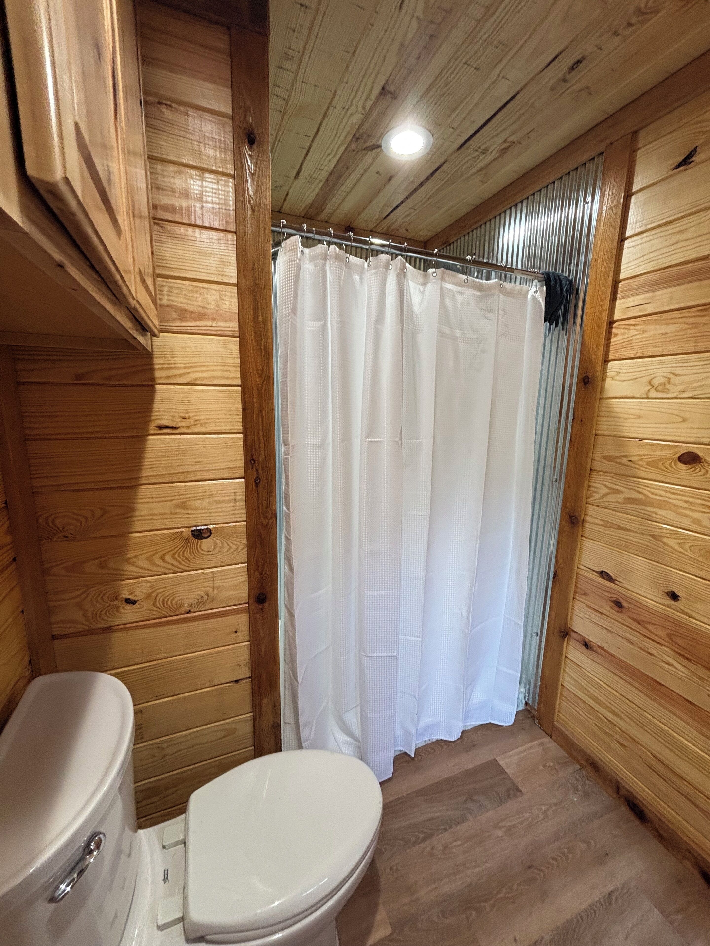 Une salle de bain rustique, située dans une cabane en bois, avec des toilettes, un rideau de douche et un plancher en bois.