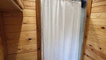 Une salle de bain rustique, située dans une cabane en bois, avec des toilettes, un rideau de douche et un plancher en bois.