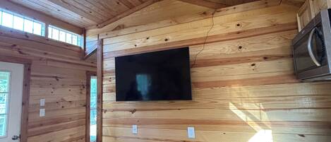 Un interior de madera con un televisor de pantalla plana montado en la pared, un horno empotrado y una puerta con ventanal.