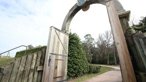 Un arco in legno con uno stemma araldico che dà accesso a un sentiero immerso nel verde.