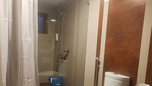 A bathroom with a white toilet, a shower, and a blue bucket. - River Meadows  (Tiruvalla)