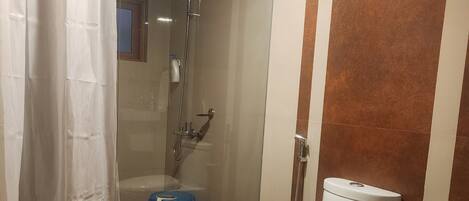 A bathroom with a white toilet, a shower, and a blue bucket.