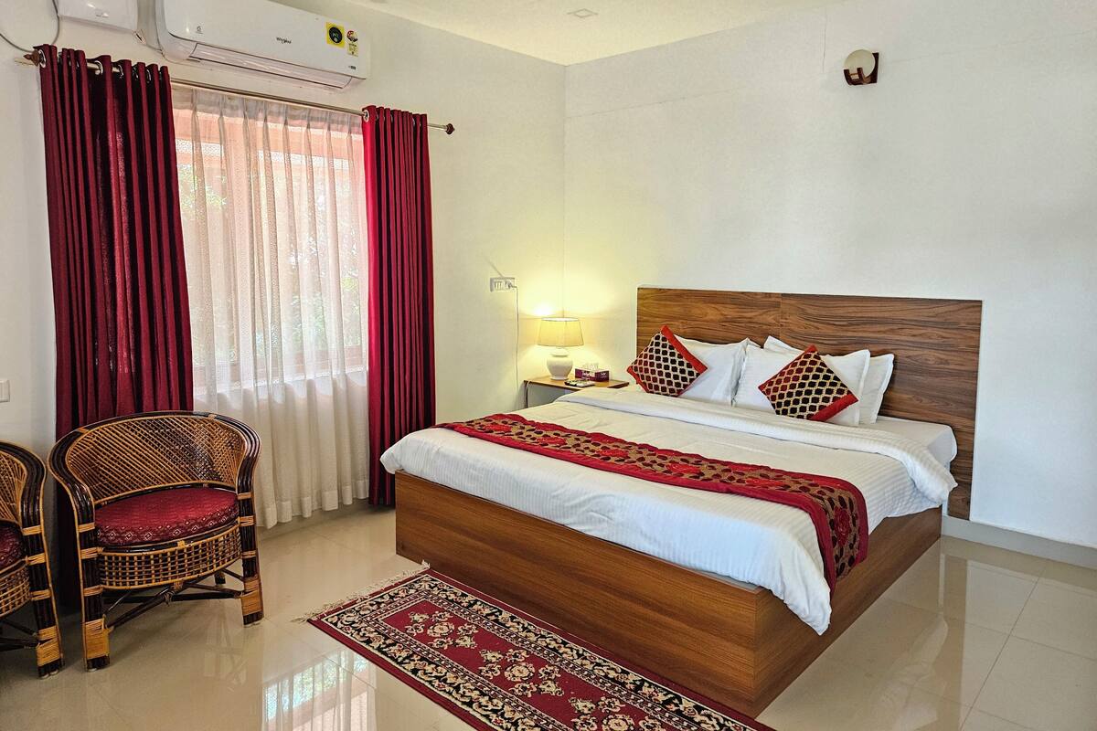 A hotel room with a bed, a chair, a nightstand, a lamp, an air conditioning unit, and a ceiling fan.