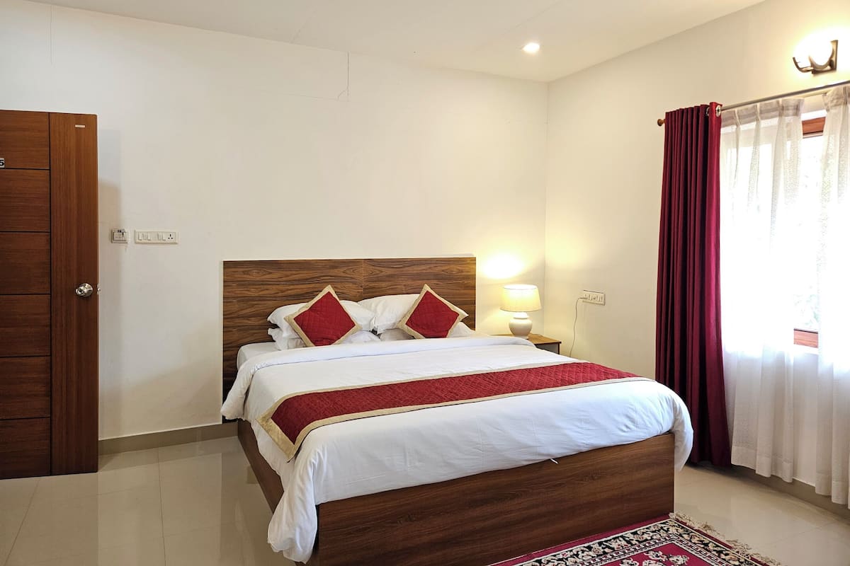A bedroom with a wooden headboard, a bed with white bedding and red accents, a bedside lamp, a red curtain, and a patterned rug.