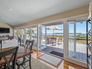 A spacious room with a large sliding glass door leading to an outdoor deck with a view of the water. - Bay Breeze - Waterfront with Boat Dock, Helipad! (Panacea)