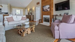 A spacious living room with a white sofa, a glass coffee table, and a wooden accent wall. - Bay Breeze - Waterfront with Boat Dock, Helipad! (Panacea)
