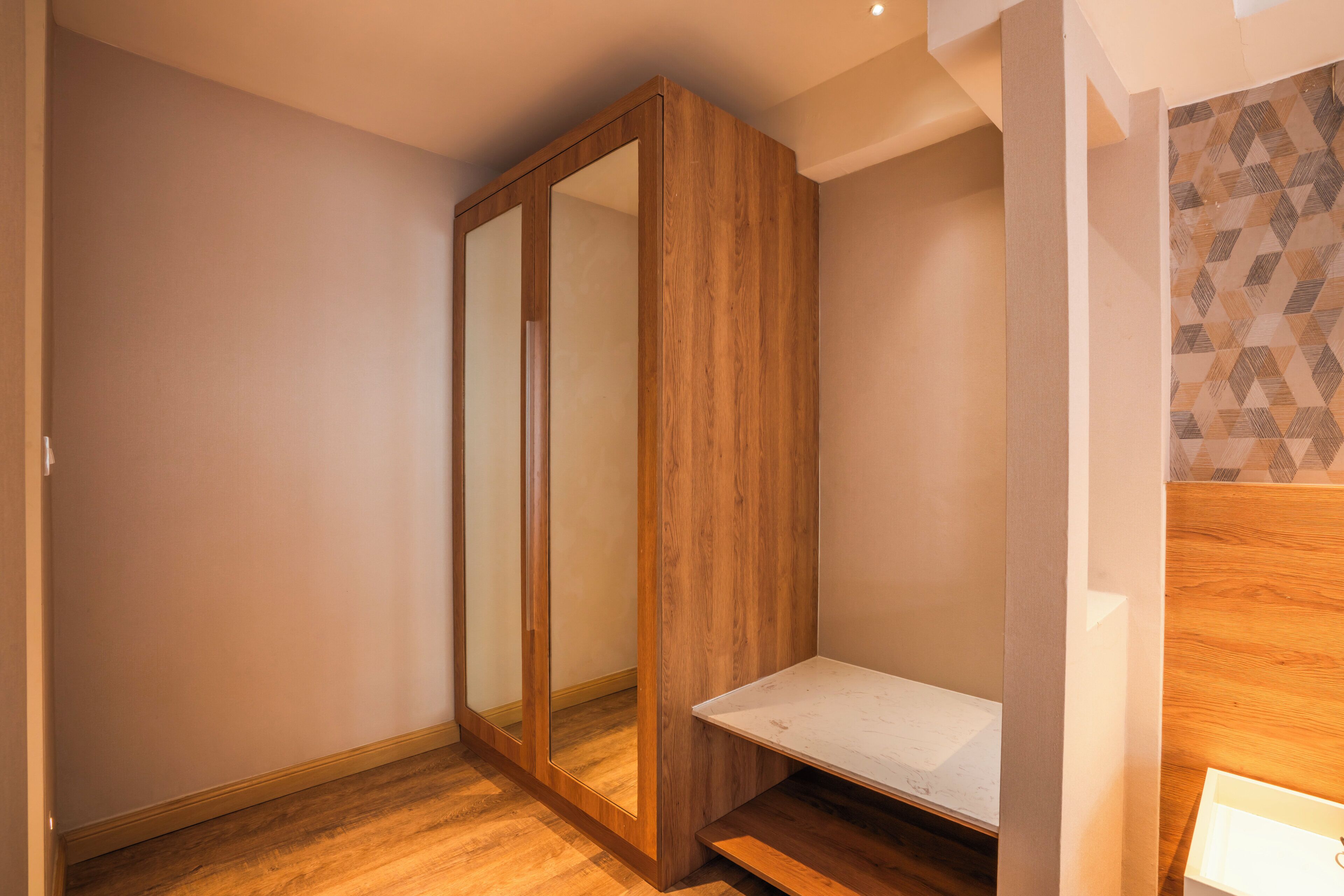 A room with a wooden wardrobe, a small white bench, and a patterned wall.