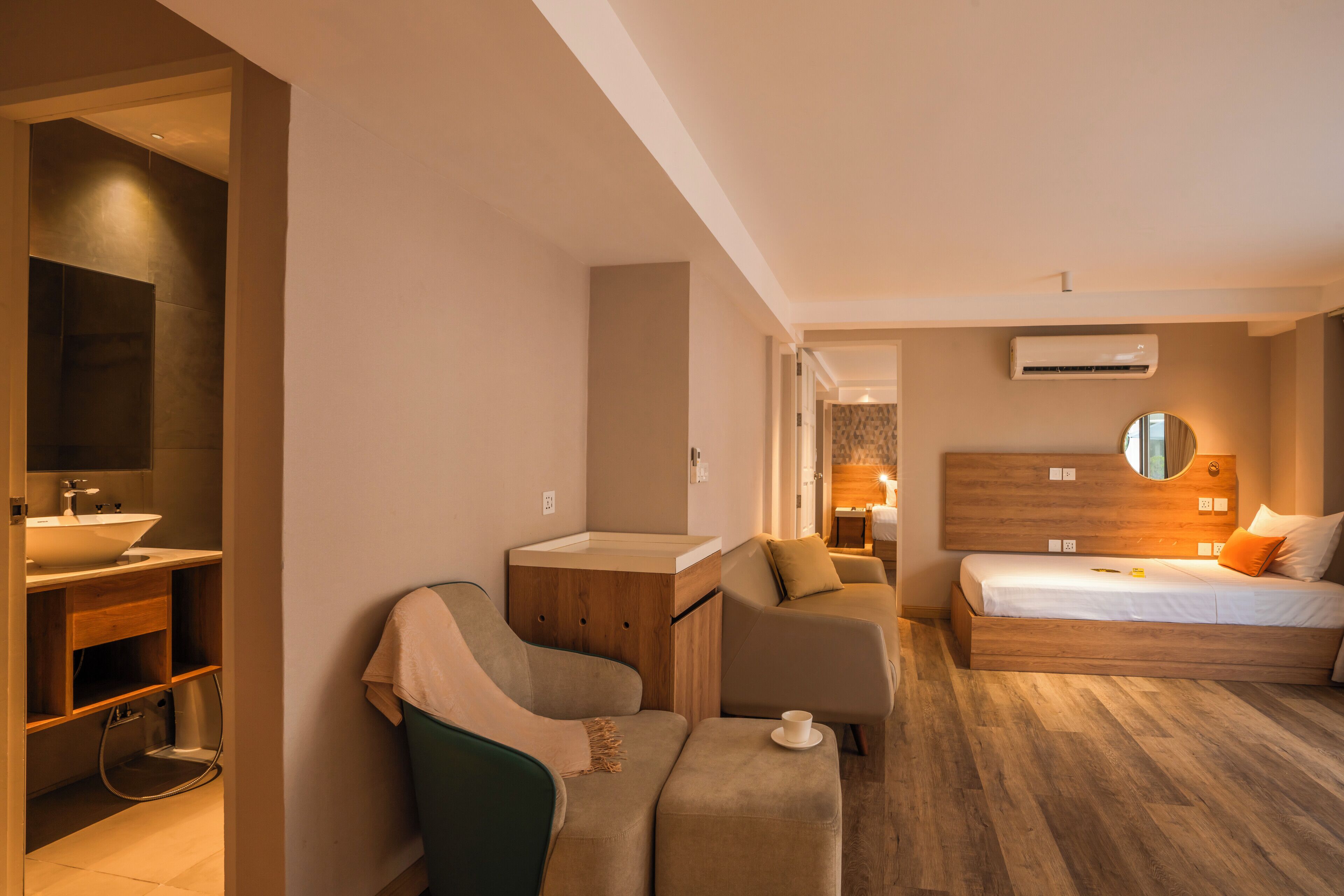 Una habitación de hotel moderna con una cama de madera, un área de descanso, un baño con lavamanos y un espejo.