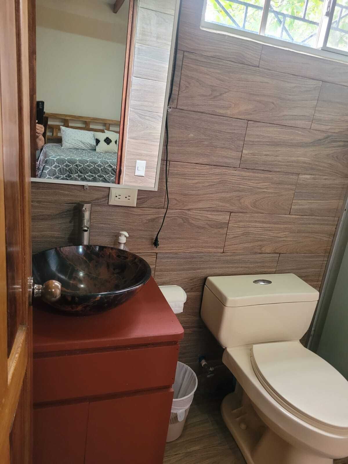 A bathroom with a wooden vanity, a marble sink, a toilet, and a mirror above the sink.