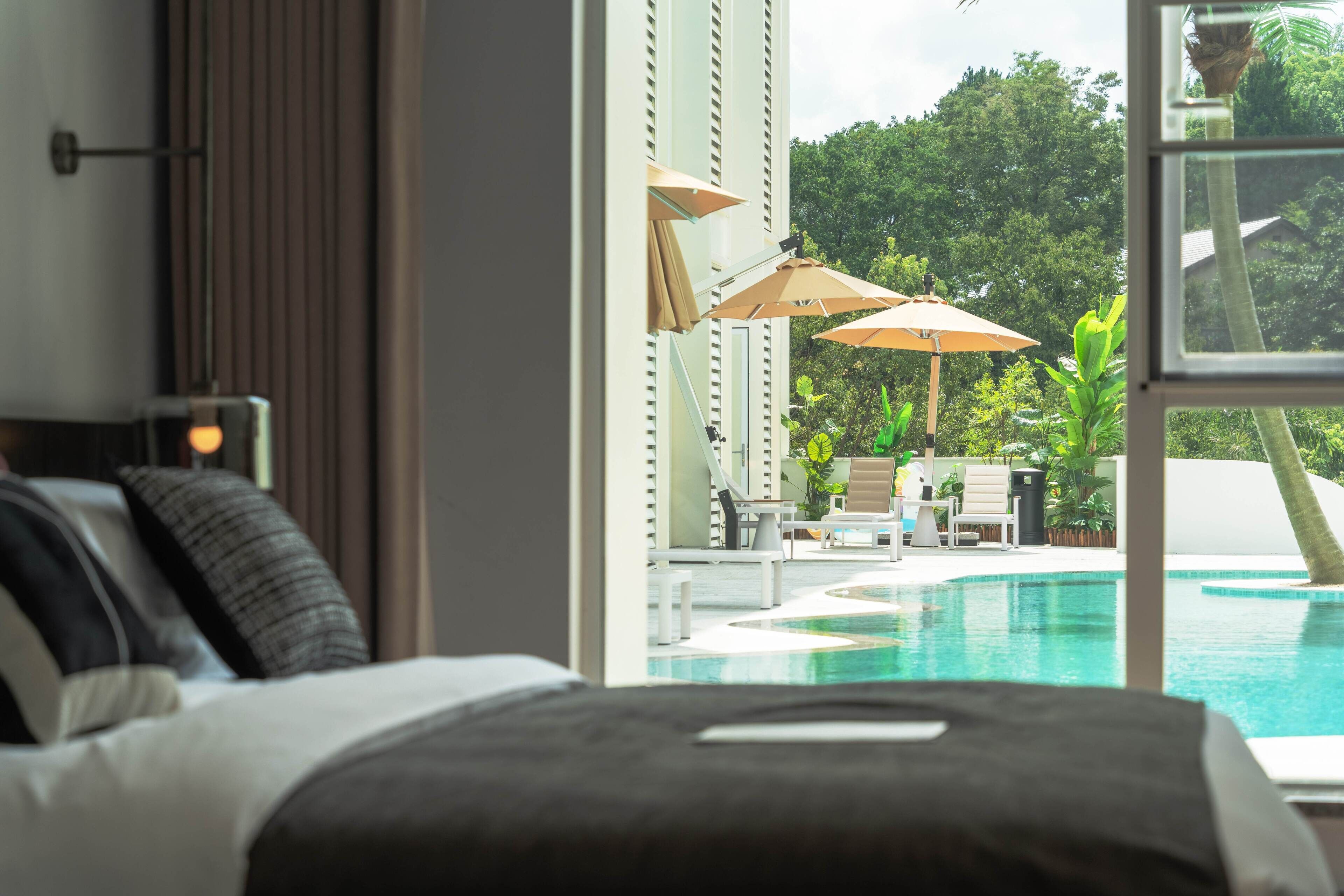 A bedroom with a view of a swimming pool and outdoor seating area.