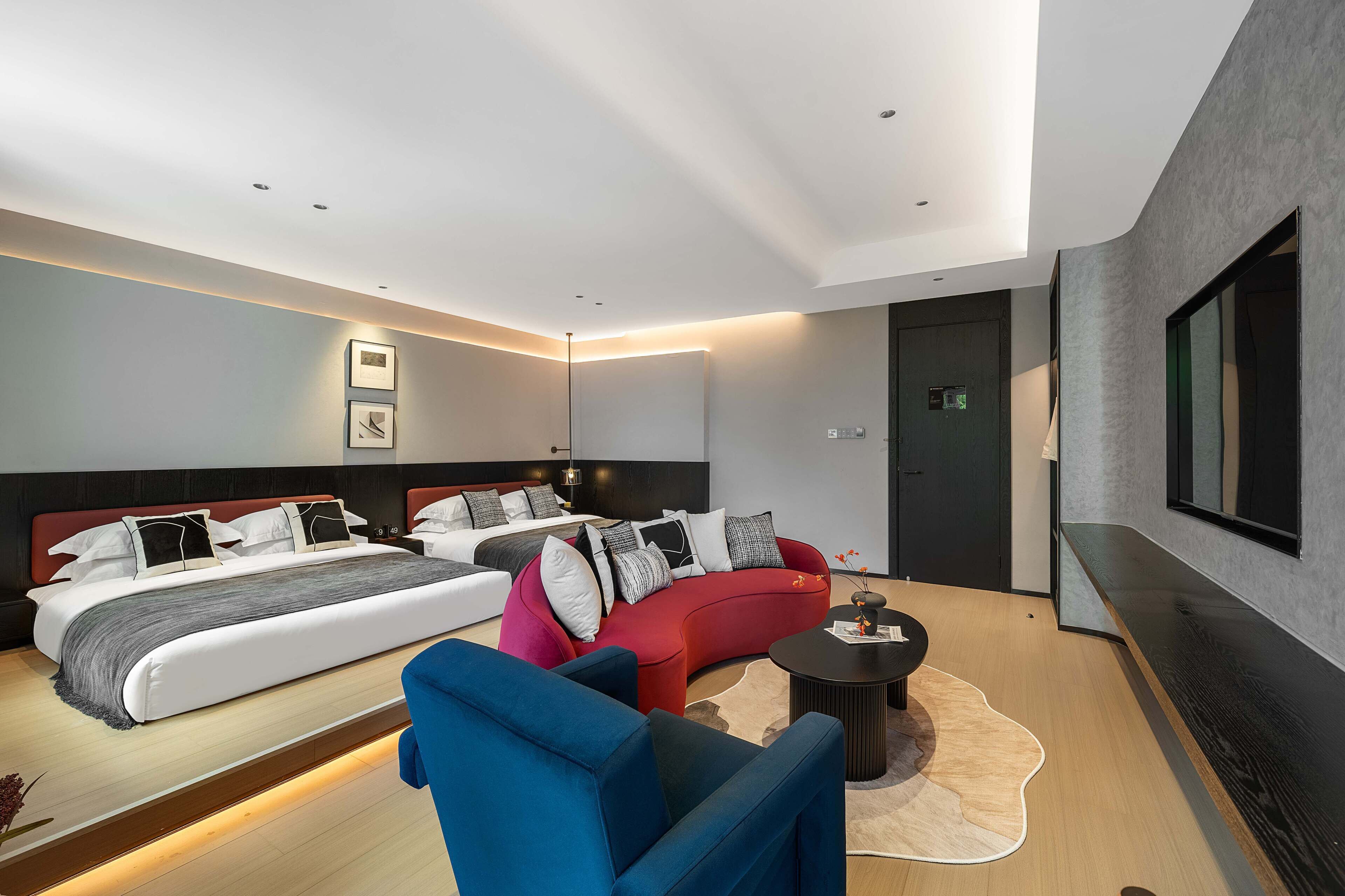 A modern hotel room with a large bed, a red sofa, a blue armchair, and a small coffee table.