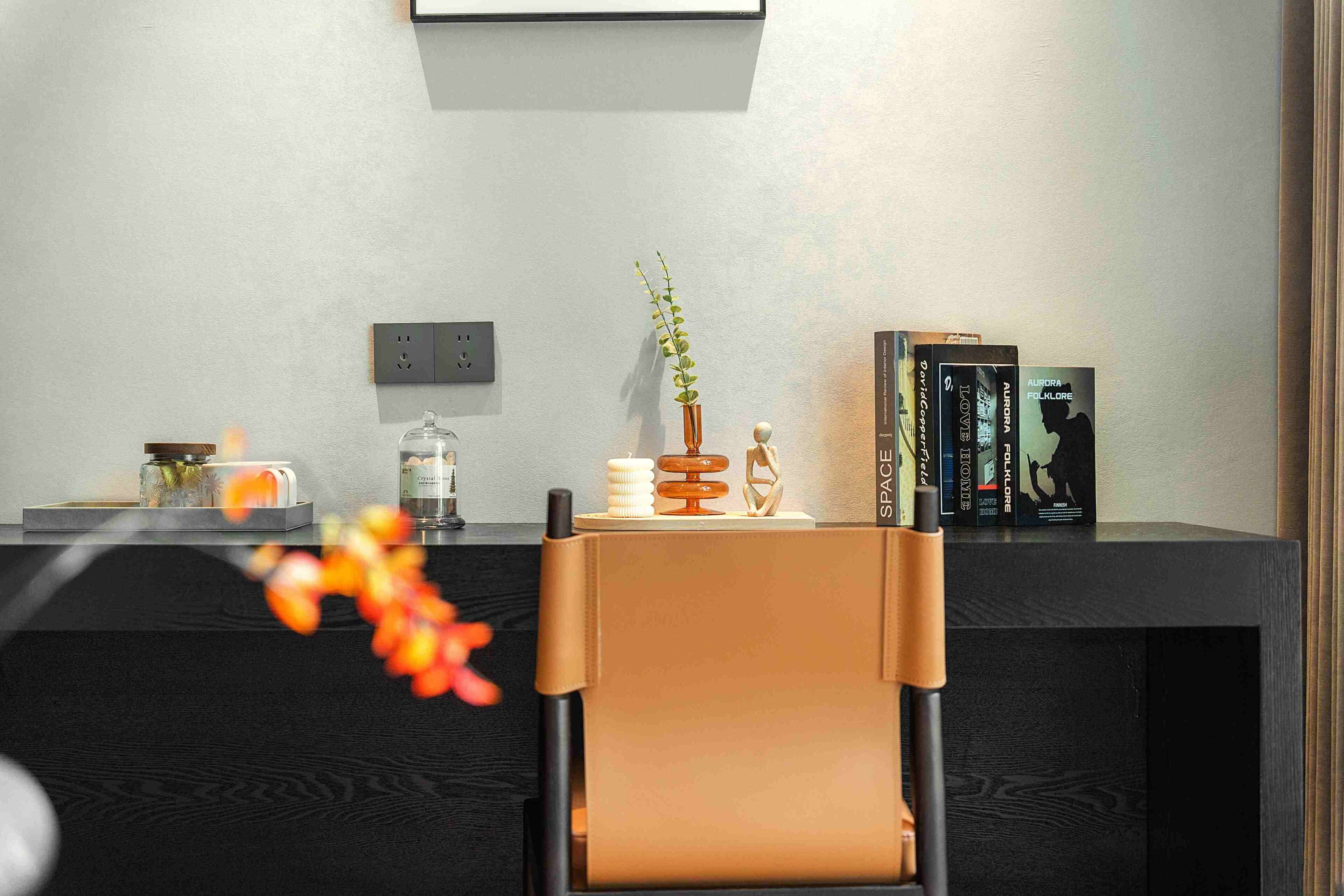 A modern office desk with a laptop, a vase with a plant, a candle, and books.
