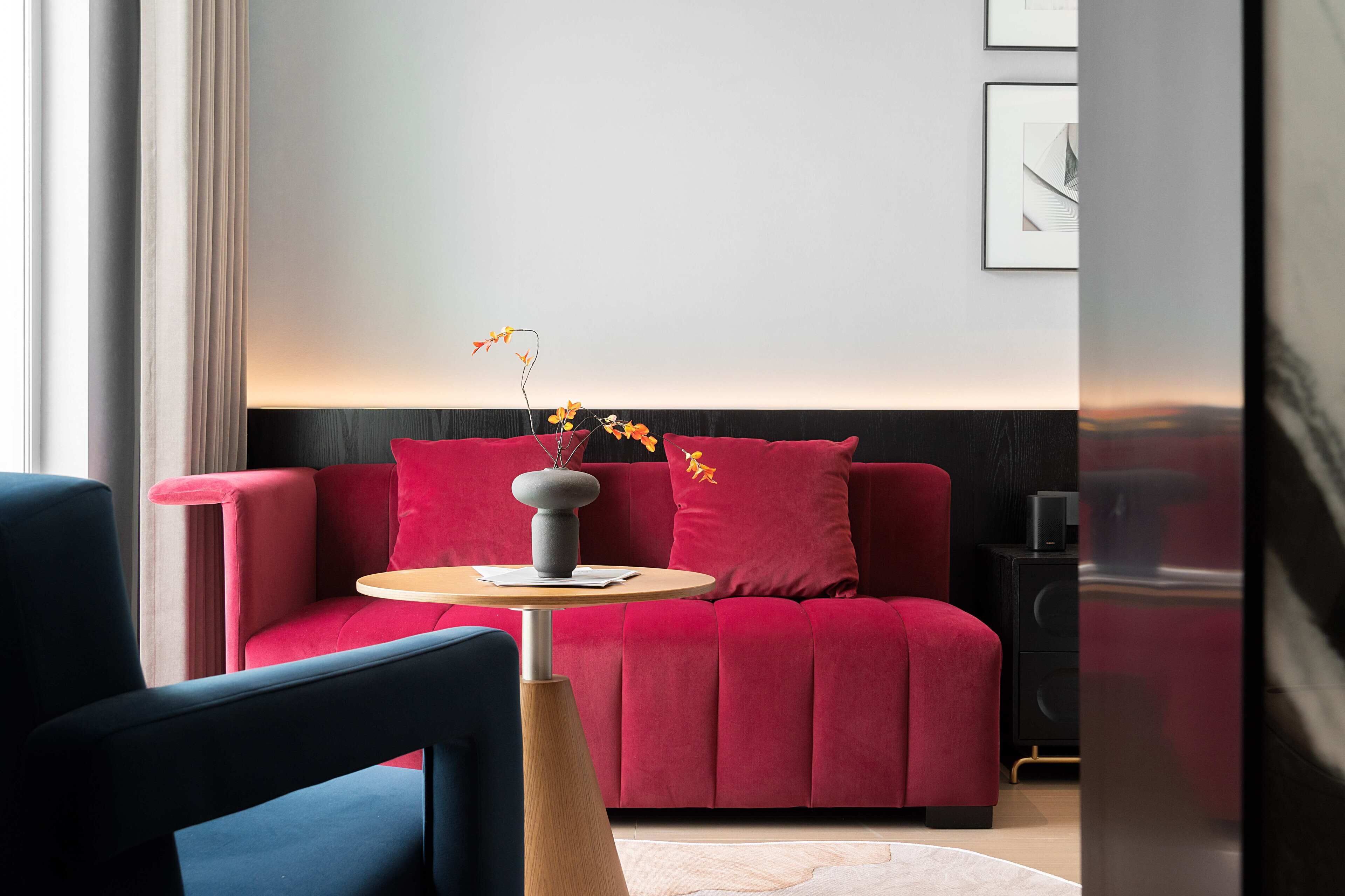Una sala moderna con un sofá rojo, una mesita redonda y un florero con flores.