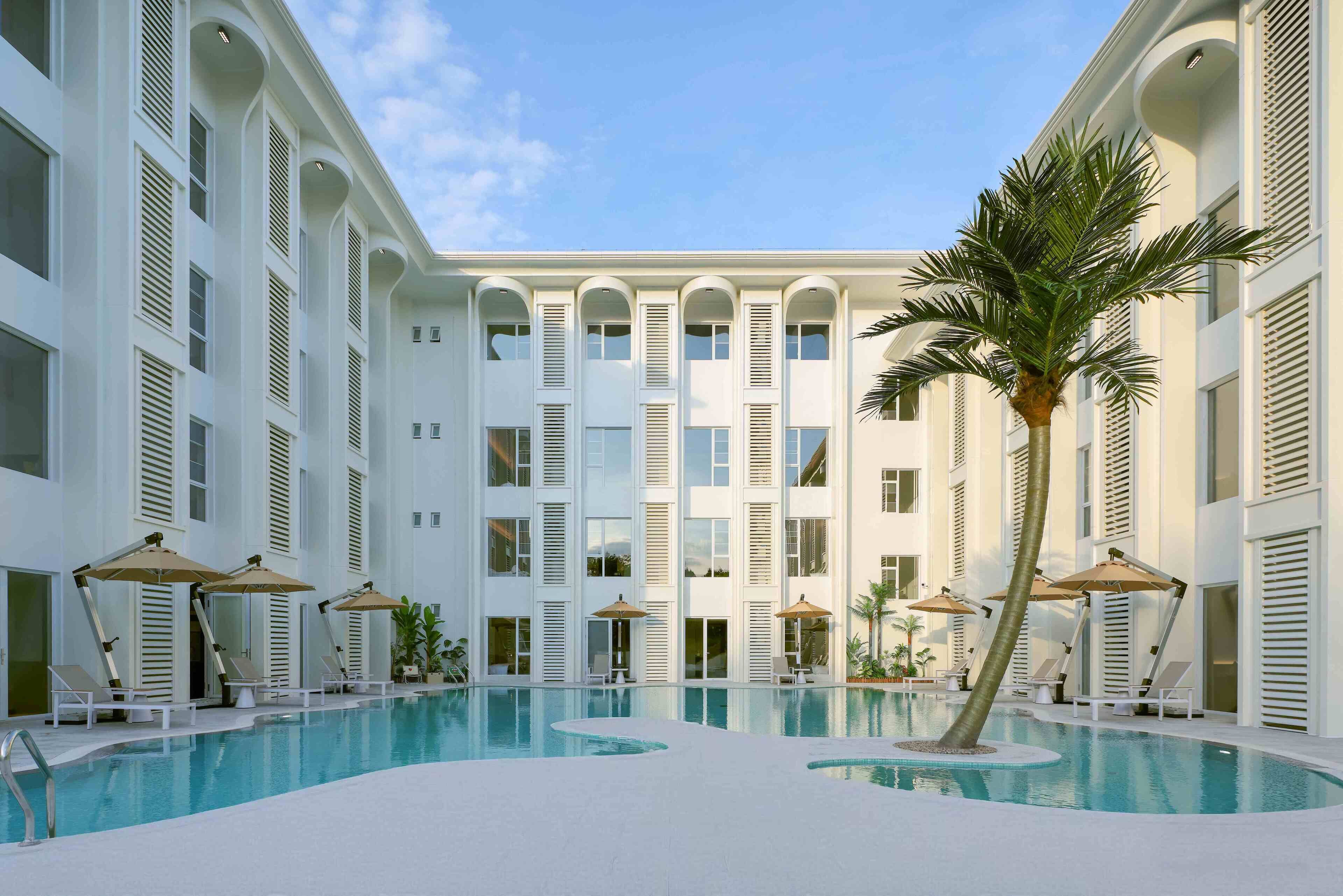 A pool area with lounge chairs and umbrellas, surrounded by a multi-story building with balconies.